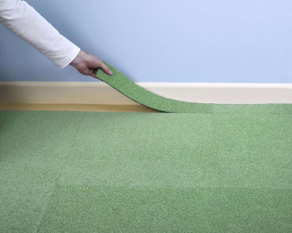 A person's arm is shown putting down Green Carpet Tile to match the rest of the carpet